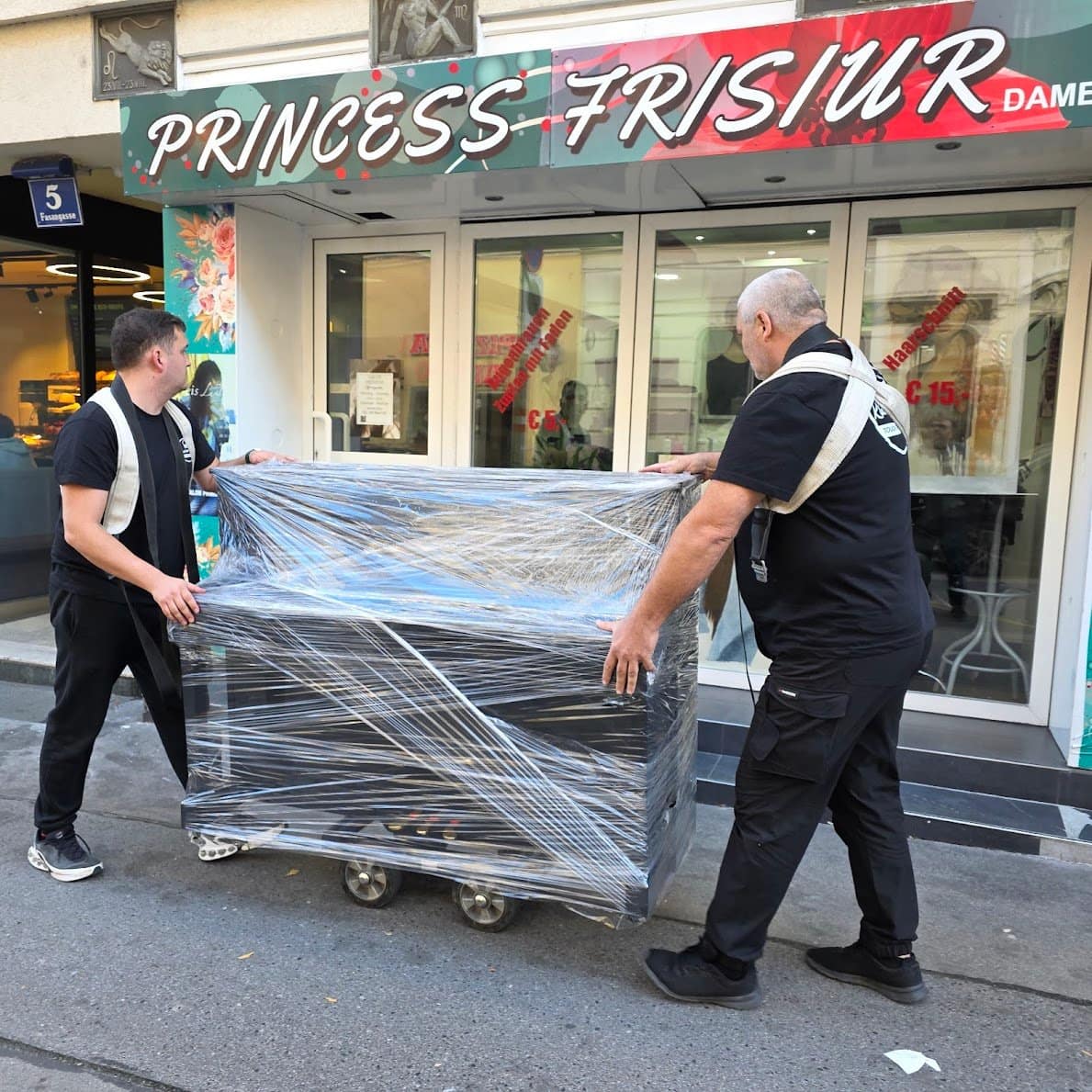 Piano transport Baden: two carriers move a wrapped piano on the dolly along a street in the town centre