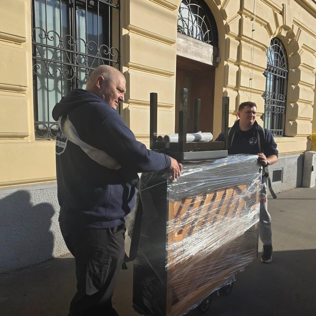 Klaviertransport Krems: verpacktes Klavier auf dem Rollwagen vor einer Altstadtfassade