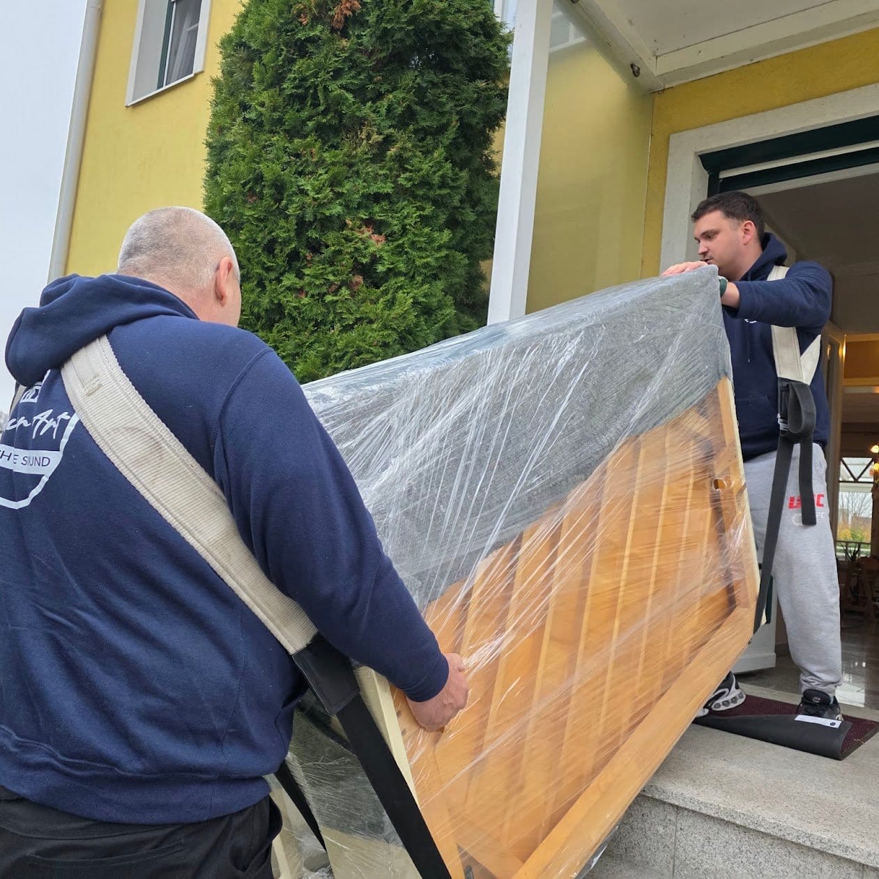 Piano transport Klosterneuburg: two carriers take a wrapped piano up the garden steps to the house