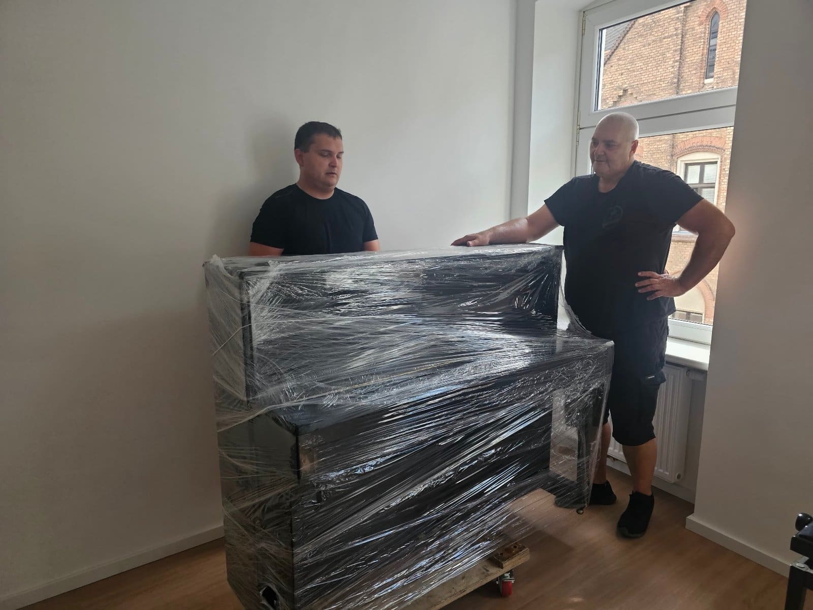 Klaviertransport Korneuburg: verpacktes Klavier in der Wohnung, zwei Träger bereit zum Abtransport