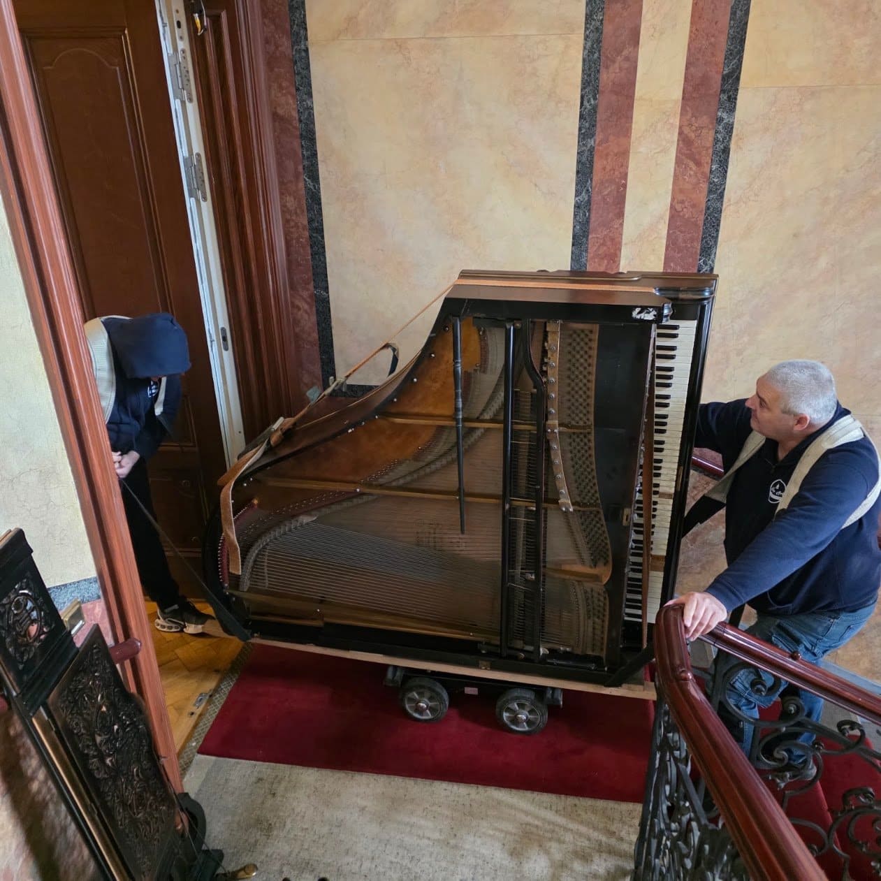Ein Flügel auf der Seite liegend auf einem Rollbrett im Stiegenhaus