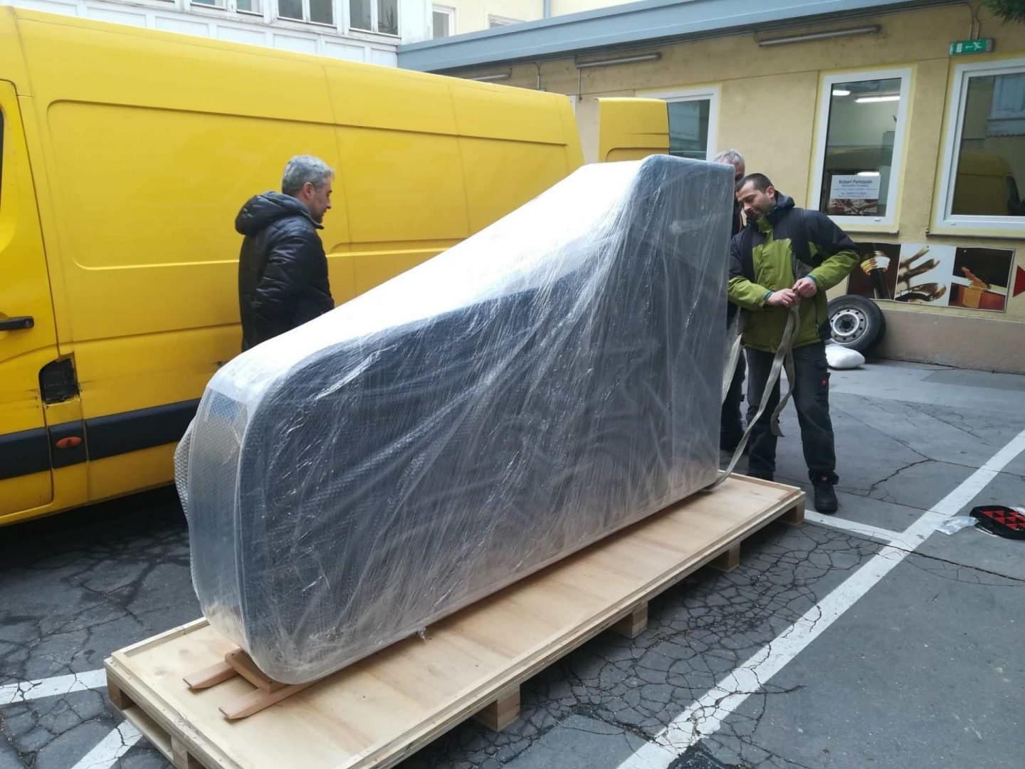 A wrapped grand piano on a pallet outdoors