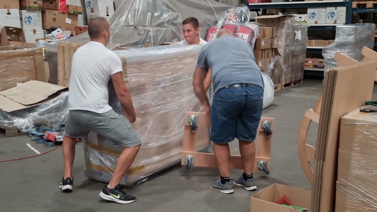 Zwei Männer verpacken ein Klavier in einer Halle